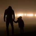 Vor einer Reihe heller Lichter zeichnen sich in der Dunkelheit die Silhouetten eines Mannes und eines Kindes ab.